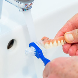 An elderly patient brushing their denture